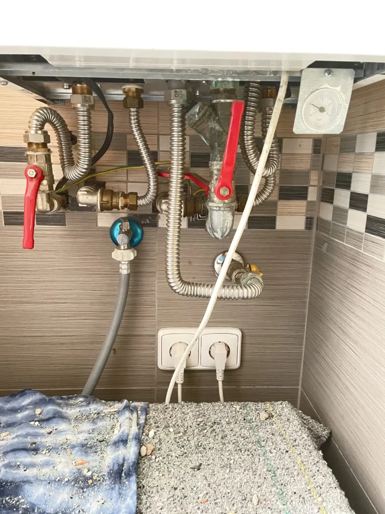 Rozvody vody a plynu pod plynovým kotlem v koupelně